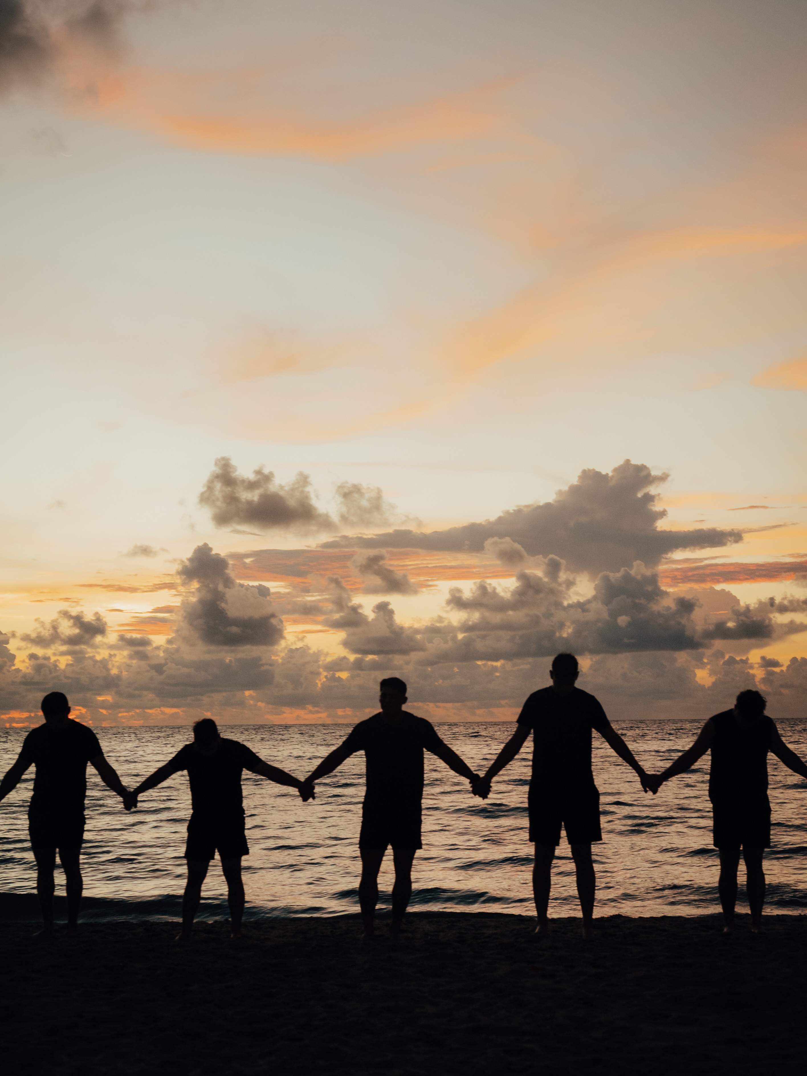 Team holding hands in a line on the beach at sunset