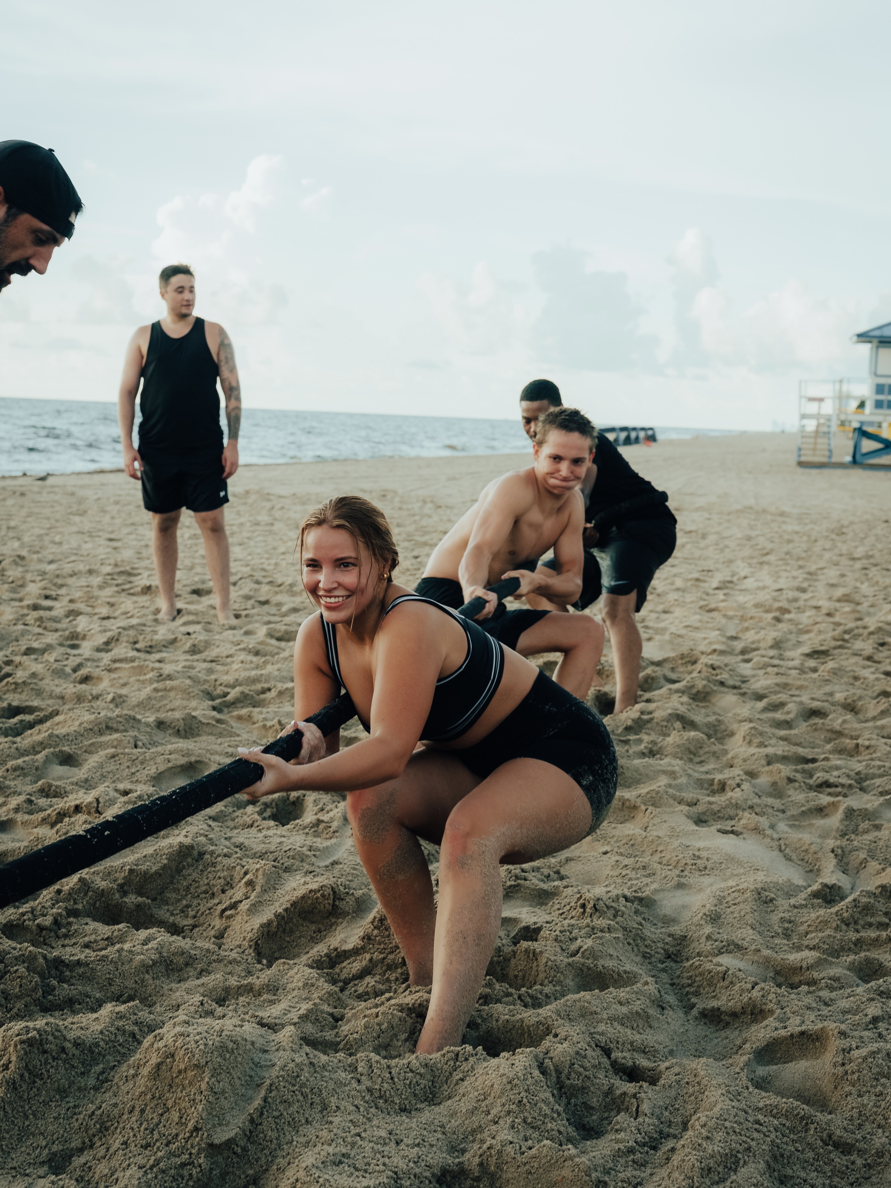 Participants pulling a rope in the sand, smiling
